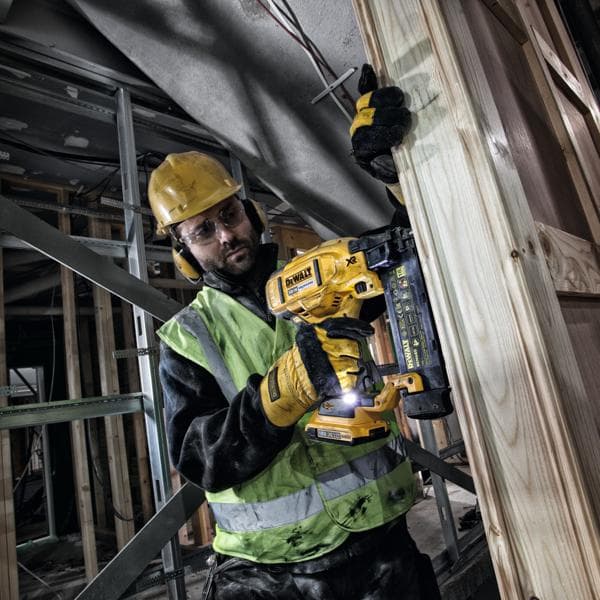 Trabalhador usa o pregador DEWALT DCN680 em estrutura de madeira, com equipamentos de segurança.