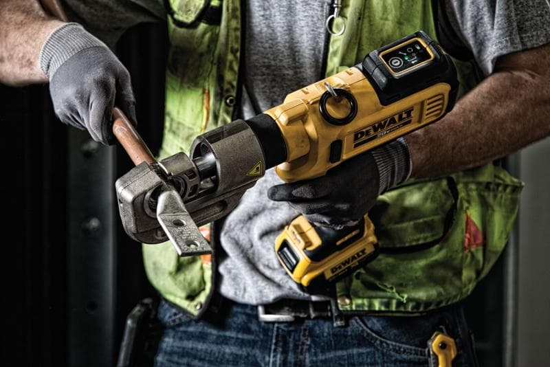 Uma pessoa utiliza uma ferramenta sem fio DEWALT para cortar uma barra de metal grossa enquanto usa luvas de trabalho e um colete de segurança verde.