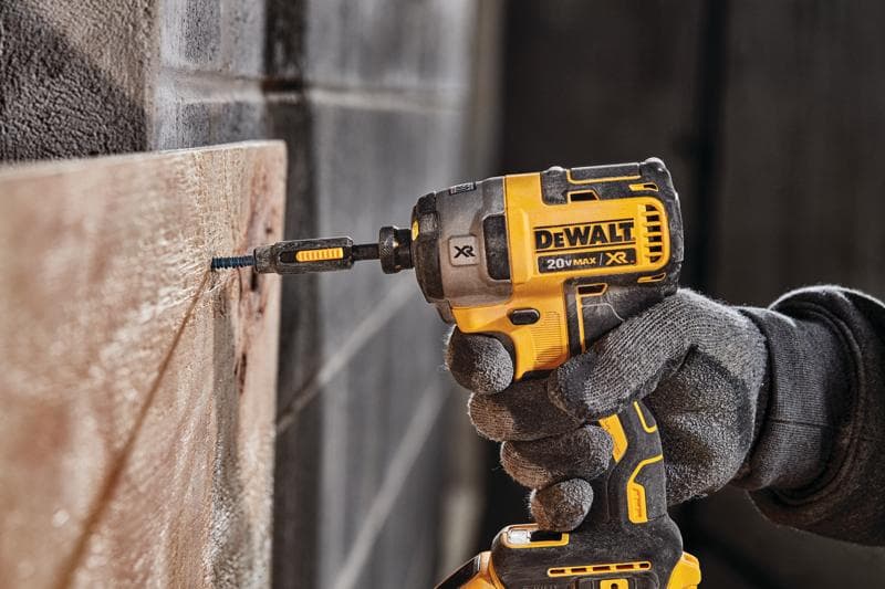 Uma pessoa usando luvas de trabalho utiliza um parafusadeira de impacto sem fio DEWALT 20V MAX XR amarela e preta para parafusar em uma tábua de madeira.