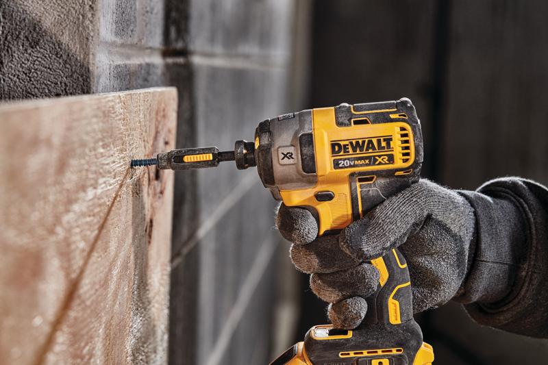 Uma pessoa usando luvas de trabalho utiliza um parafusadeira de impacto sem fio DEWALT 20V MAX XR amarela e preta para parafusar em uma tábua de madeira.